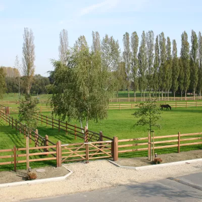 Een dubbele houten poort als toegang tot een pad met veel velden ernaast omheind met houten omheiningen van 3 rails