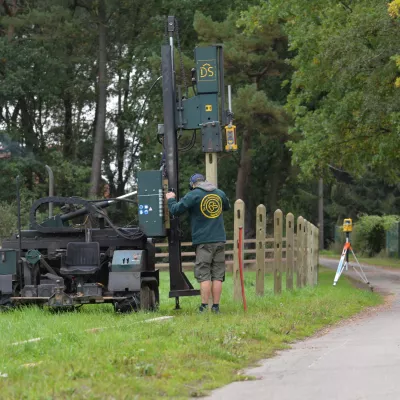 Een man installeert houten omheiningen met een palen-trilmachine