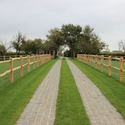 Een pad tussen gekloofde kastanjehouten omheiningen met 2 rails, vierkante palen en een gaashekwerk erop