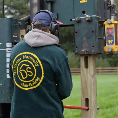 Een man installeert houten omheiningen met een palen-trilmachine